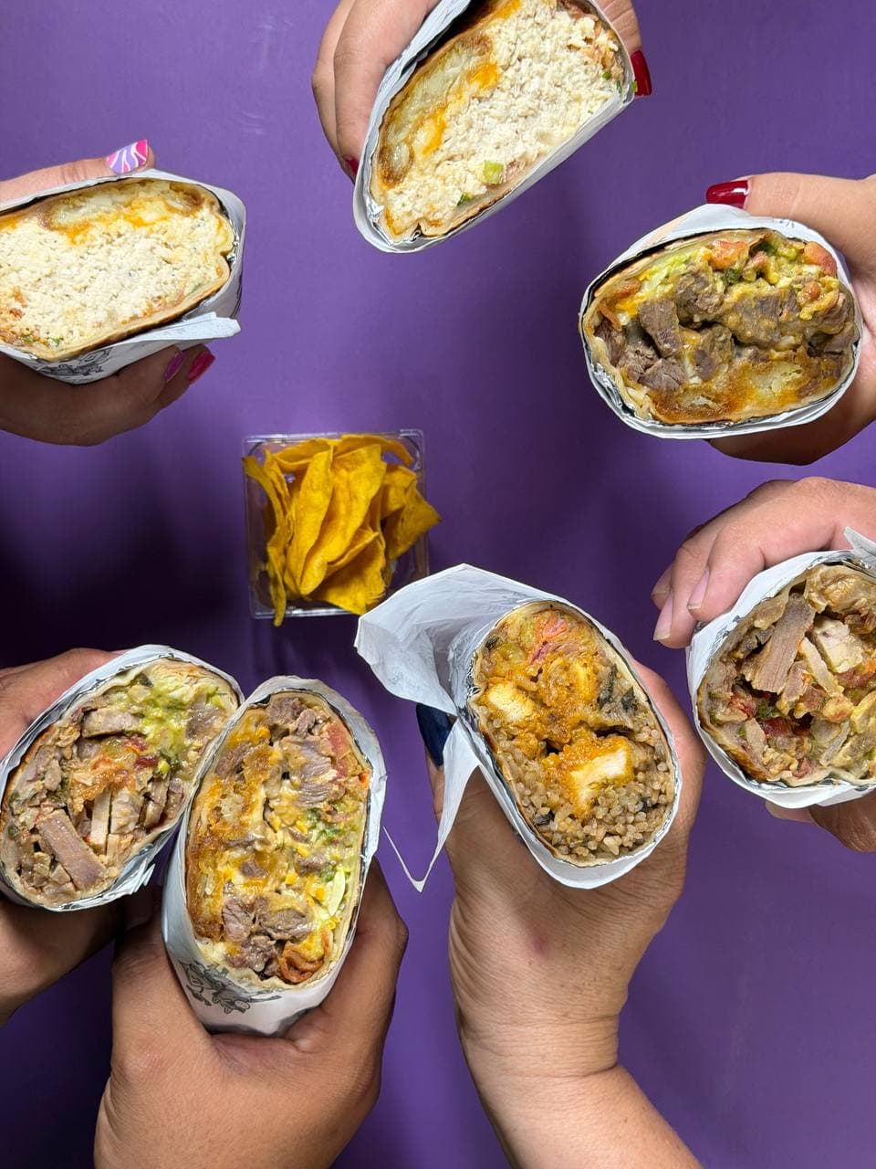 Seis manos sosteniendo distintos burritos de La Burrada